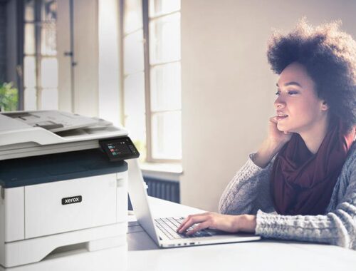 Junge Frau, die an ihrem Computer neben einem Multifunktionsdrucker Xerox® B315 arbeitet.